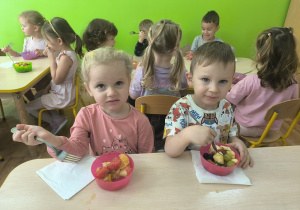 dzieci jedzą wykonaną sałatkę owocową