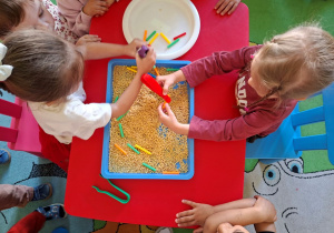 dzieci szukają ukrytych słomek w kaszy