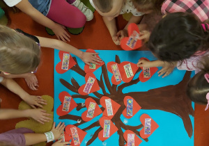 dzieci przyklejają swoje serduszka na drzewie